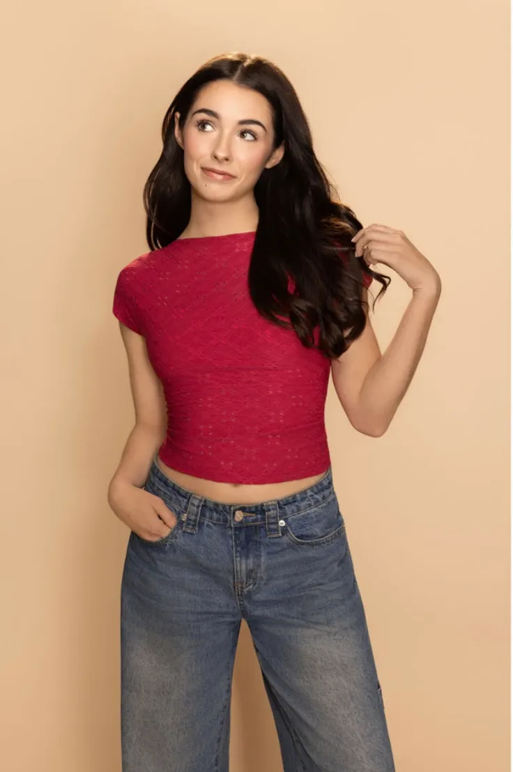 Elisabeth Fitzgerald, three-quarter length in a red top, one hand in her hair, glancing upward